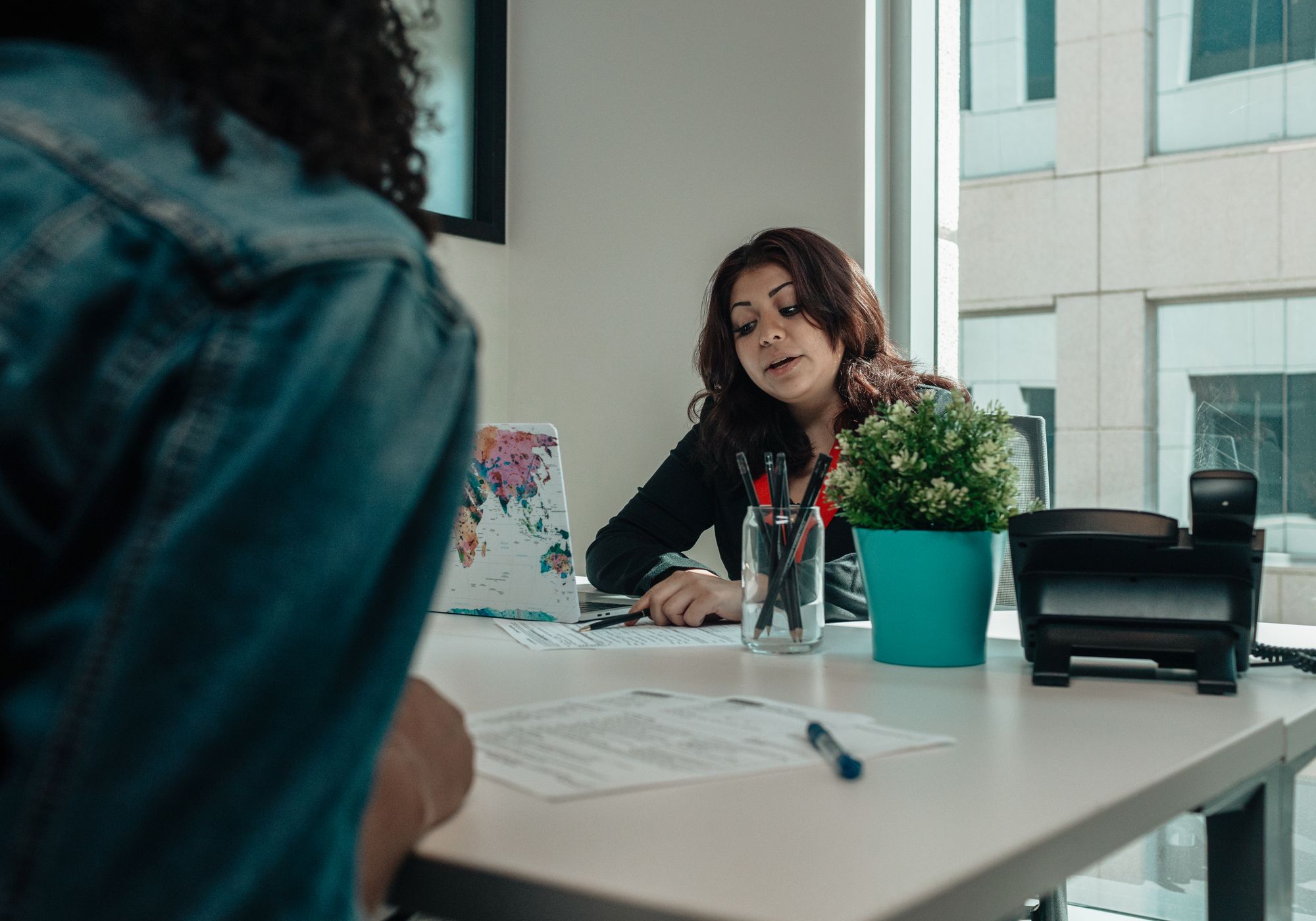 A caseworker at her desk in conversation with someone seated opposite, paperwork between them.